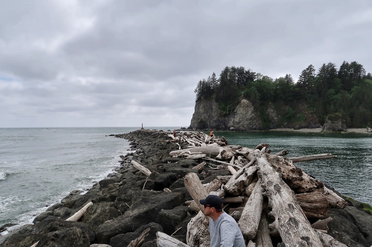 man sitting on rock and driftwood jetty with James Island in the background