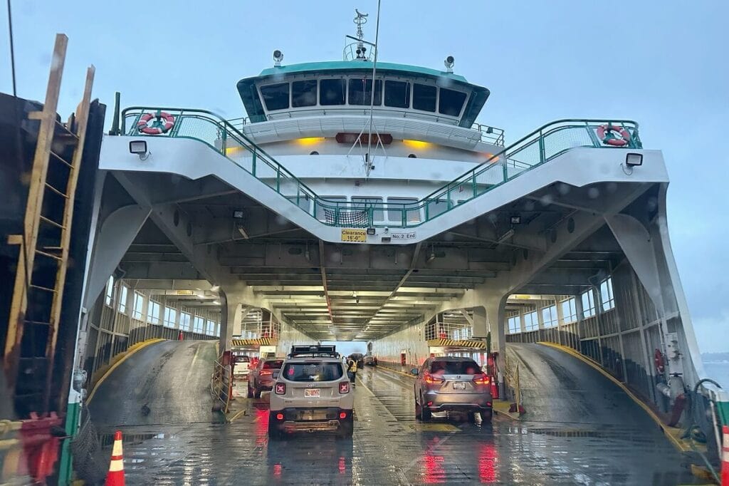 Vehicles boarding the Bainbridge Island ferry on a wet deck, early evening