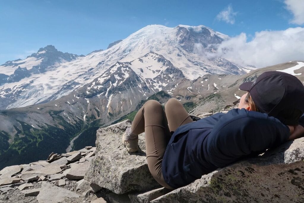 A hiker rests laying on rocks while looking out toward a dramatic mountain scene.