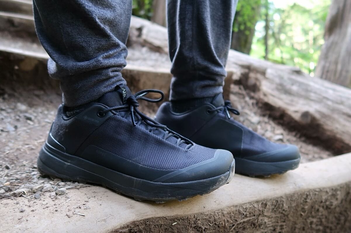 The best shoes for Olympic National Park shown in close-up, featuring black Gore-Tex material and rugged soles, worn by a hiker on a forest trail with wood steps and dirt.