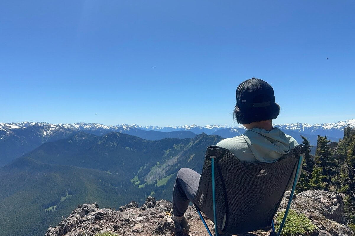 Visiting Hurricane Ridge in Olympic National Park means soaking in panoramic views like this, where a hiker relaxes in a camp chair overlooking endless forested ridges and snow-capped peaks. 
