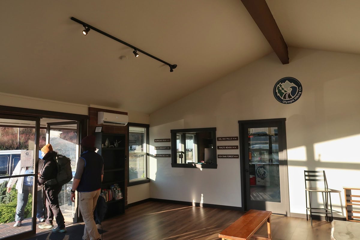 Visitors in winter hiking gear gather near the entrance of the Olympic Hiking Co building. Inside are trail signs pointing toward Olympic National Park destinations.